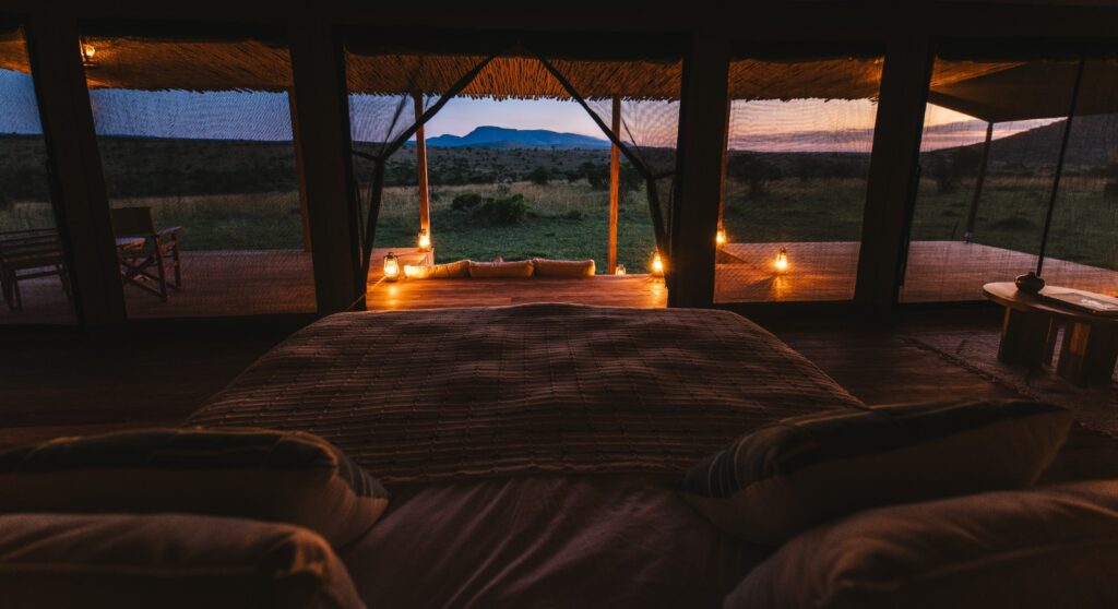 Luxury safari tent bedroom at Little Enkewa illuminated by lanterns at dusk in the Masai Mara